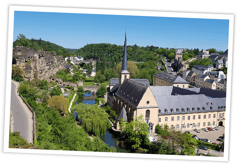 Panoramablick auf die Altstadt von Luxemburg mit dem Fluss Alzette und historischen Klostergebäuden im grünen Tal.