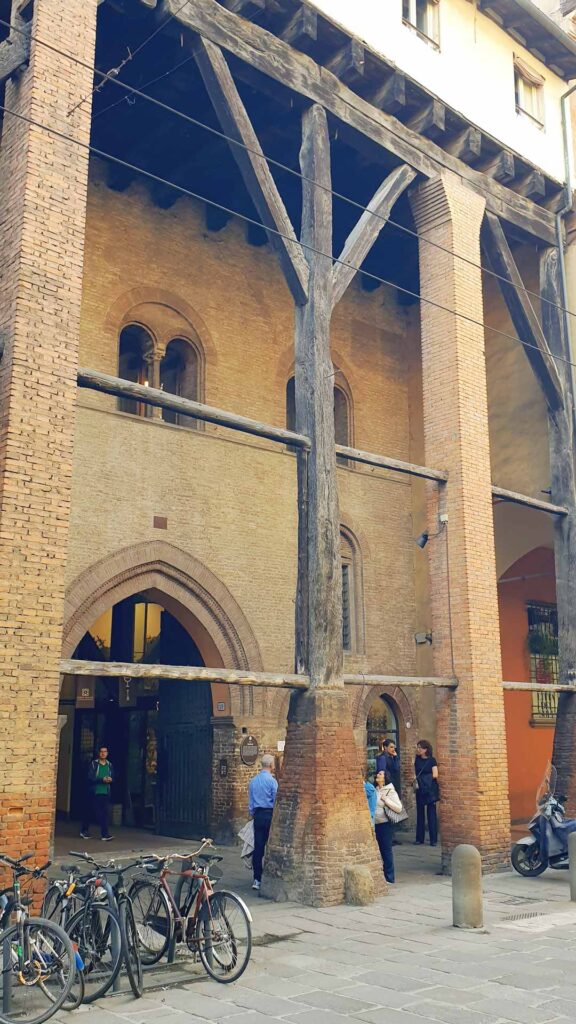 Hohe mittelalterliche Holzpfeiler und Backsteinfassade des Casa Isolani mit geparkten Fahrrädern davor in Bologna.