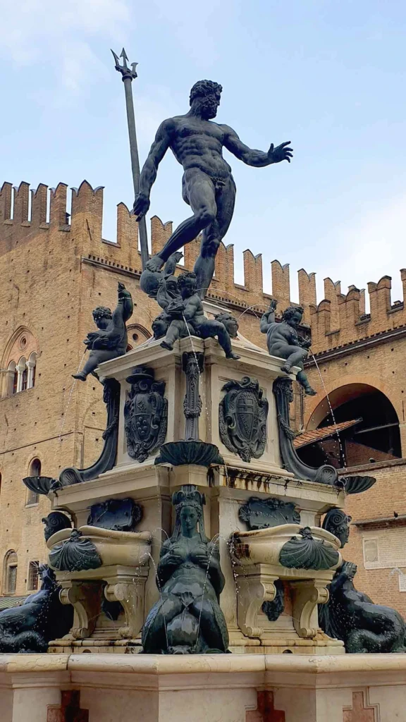 Der Neptunbrunnen mit der Bronzestatue des Neptun und Wasserspeiern vor der historischen Backsteinfassade des Palazzo Re Enzo in Bologna.