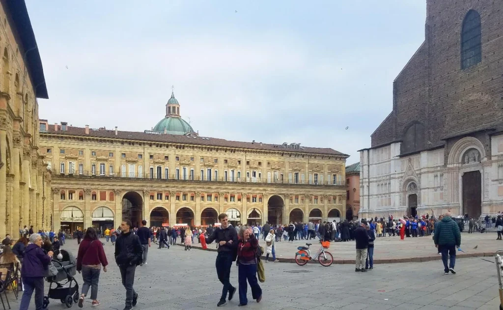 Belebte Piazza Maggiore in Bologna mit der charakteristischen Backsteinfassade der Basilika San Petronio und dem Palazzo dei Banchi.