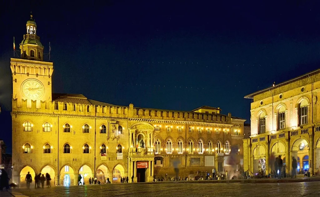 Stimmungsvoll beleuchteter Palazzo d'Accursio mit Uhrenturm an der Piazza Maggiore in Bologna bei Nacht.