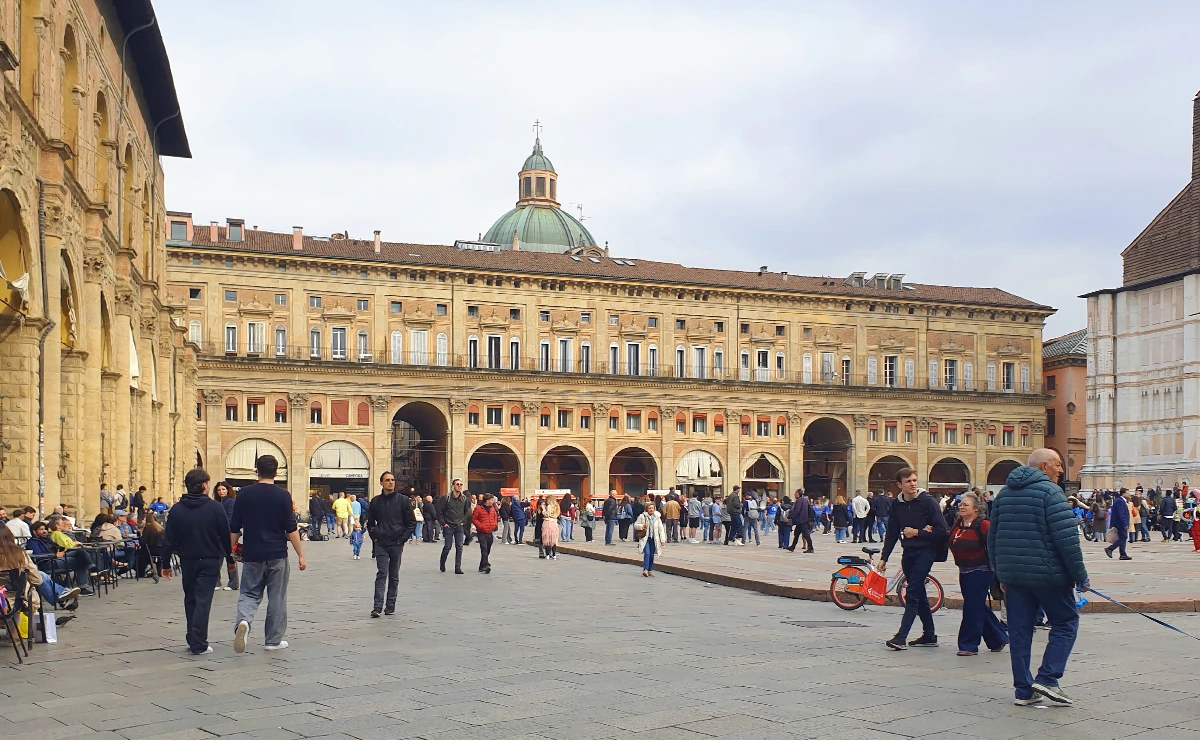 Belebter Blick über die Piazza Maggiore in Bologna mit historischen Backsteingebäuden und den berühmten Portici unter bedecktem Himmel – ein Highlight der Bologna Sehenswürdigkeiten.