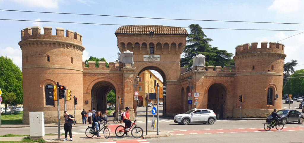 Das historische Backstein-Stadttor Porta Saragozza in Bologna mit zwei runden Türmen und Radfahrern im Vordergrund.