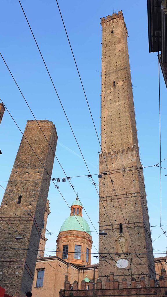 Blick von unten auf die zwei geschlechtertürme Torre Asinelli und den schiefen Torre Garisenda in Bologna unter blauem Himmel.