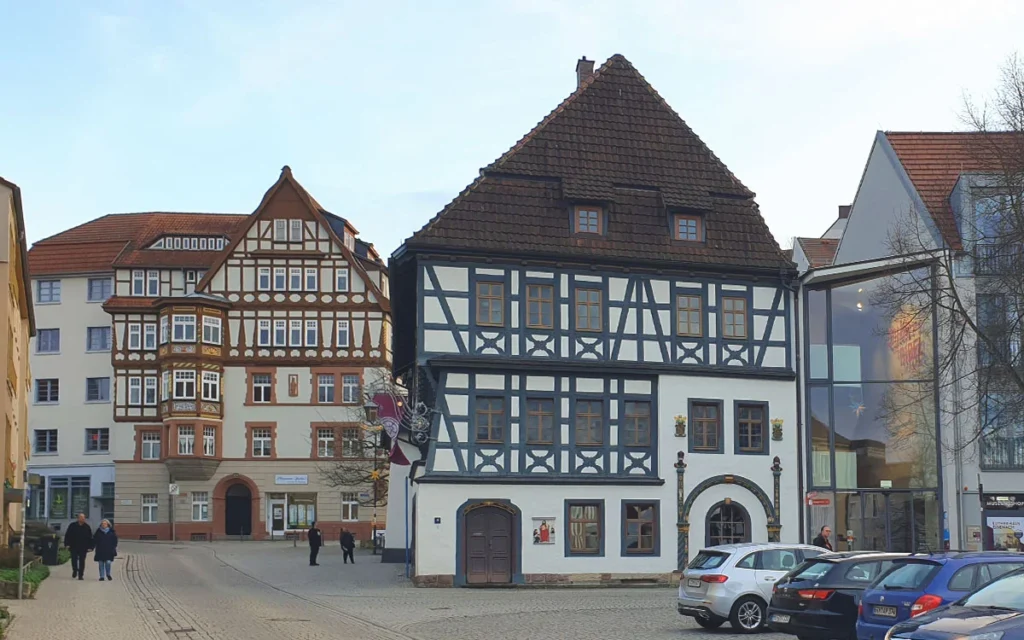 Das historische Lutherhaus mit imposantem Fachwerk in Eisenach, flankiert von einem modernen Glasanbau und weiteren Altstadt-Fachwerkgebäuden.