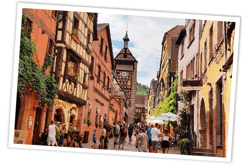 Typische malerische Fachwerkhäuser in einer engen Gasse im Elsass, Frankreich, mit Besuchern vor den historischen Gebäuden.