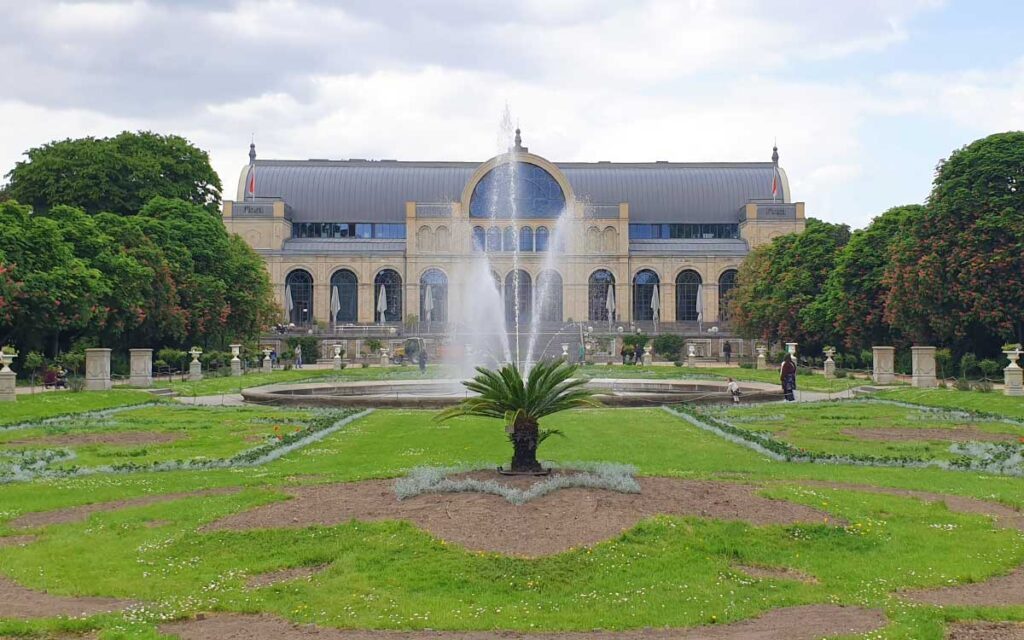 Das historische Festhaus der Flora in Köln mit einer großen Wasserfontäne und gepflegten Grünflächen im Botanischen Garten.