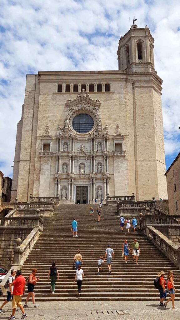 Die beeindruckende breite Steintreppe vor der Kathedrale von Girona mit Besuchern und Touristen an einem sonnigen Tag.