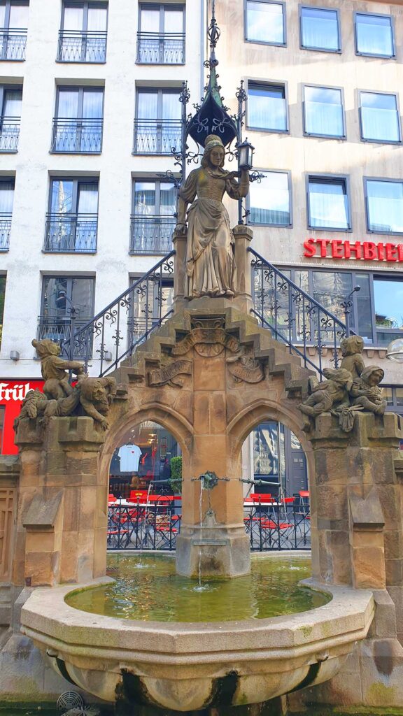 Historischer Heinzelmännchenbrunnen in der Kölner Altstadt mit der Figur der Schneiderfrau und kleinen Wichteln.