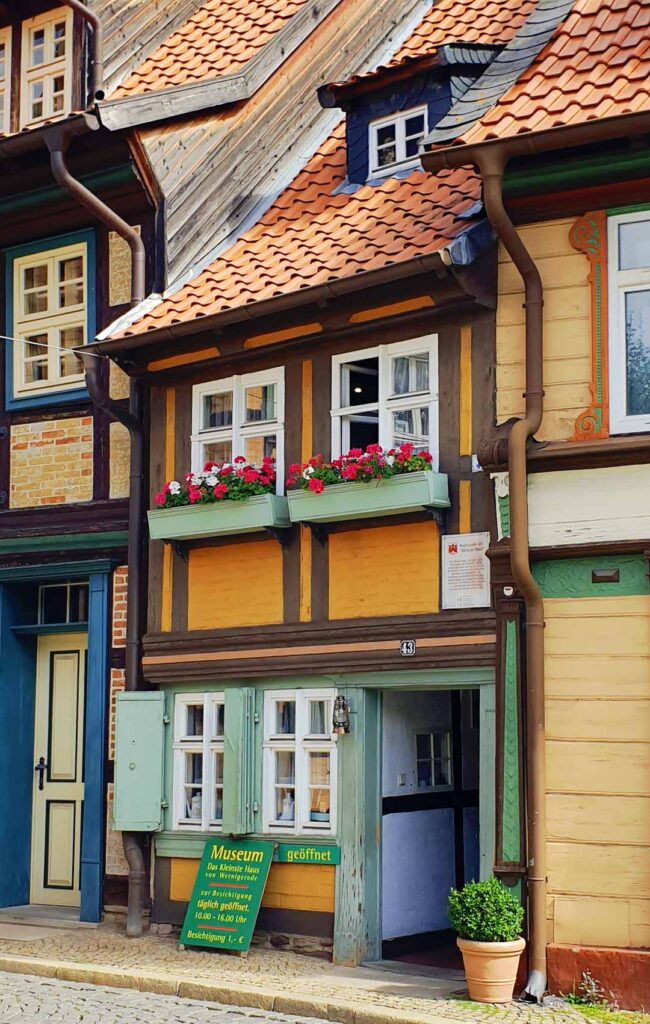 Das Kleinste Haus von Wernigerode mit blassgrünen Fensterläden, roten Blumenkästen und geöffneter Eingangstür