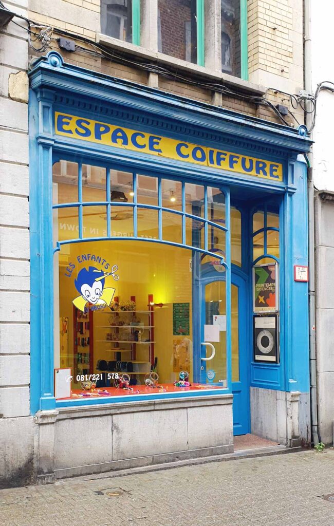Jugendstil-Fassade eines Friseursalons für Kinder namens "Les Enfants d'Abord" mit blauer Holzverkleidung und geschwungenen Fenstern in Namur