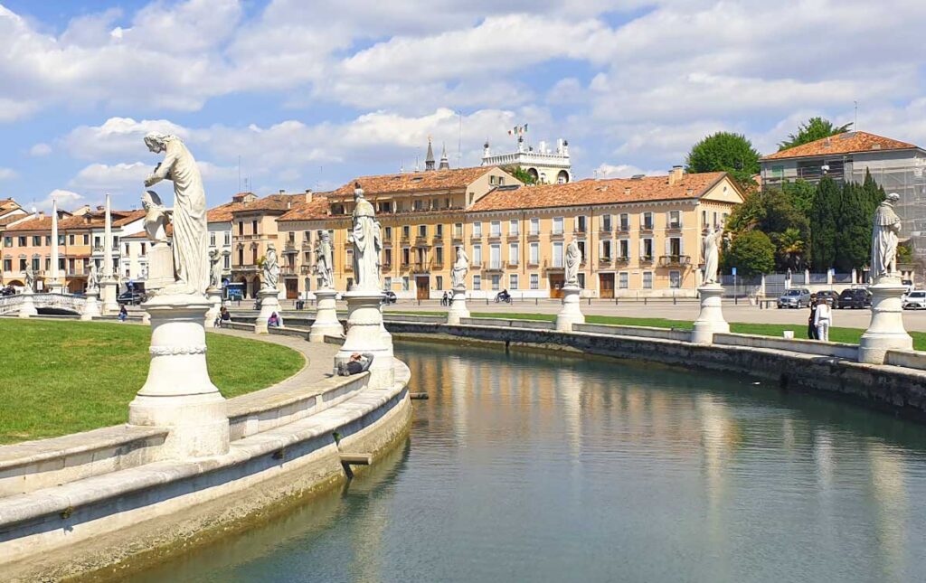 Der Prato della Valle in Padua mit seinem Wasserkanal, den weißen Statuen und historischen Gebäuden im Hintergrund.