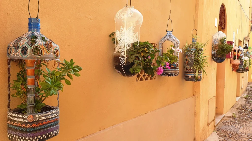 Blumenampeln aus Plastikflaschen an einer orangenen Fassade