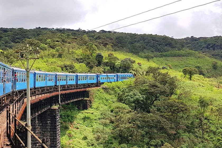 Blauer Zug in Sri Lanka schlängelt sich über eine Steinbrücke durch das grüne Hochland zwischen Kandy und Ella.
