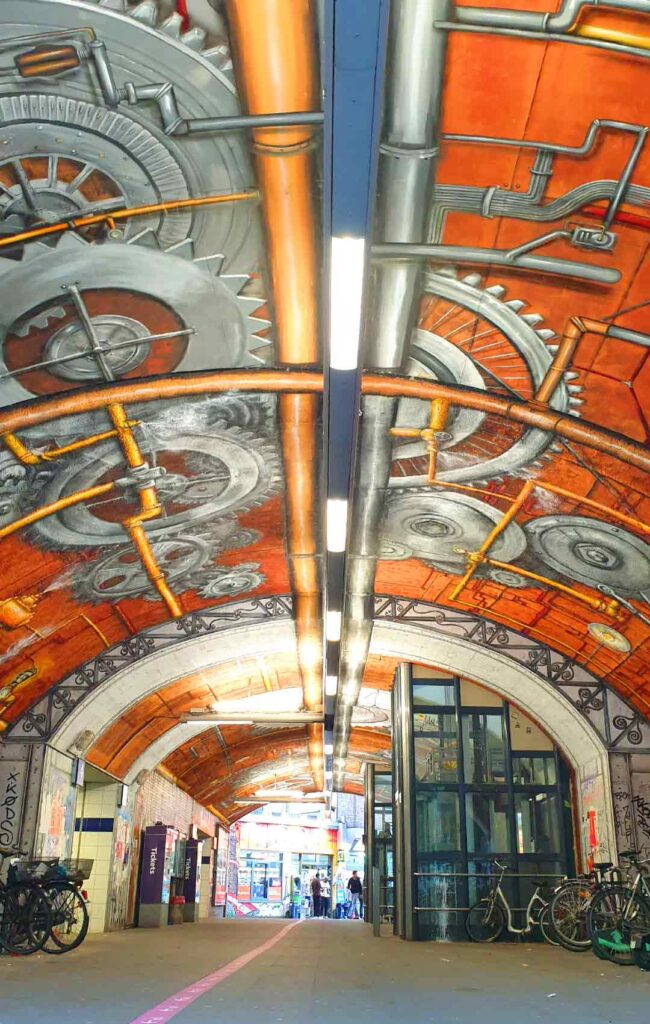 Buntes Steampunk-Graffiti mit riesigen Zahnrädern an der Decke der Bahnhofs-Unterführung in Köln-Ehrenfeld.