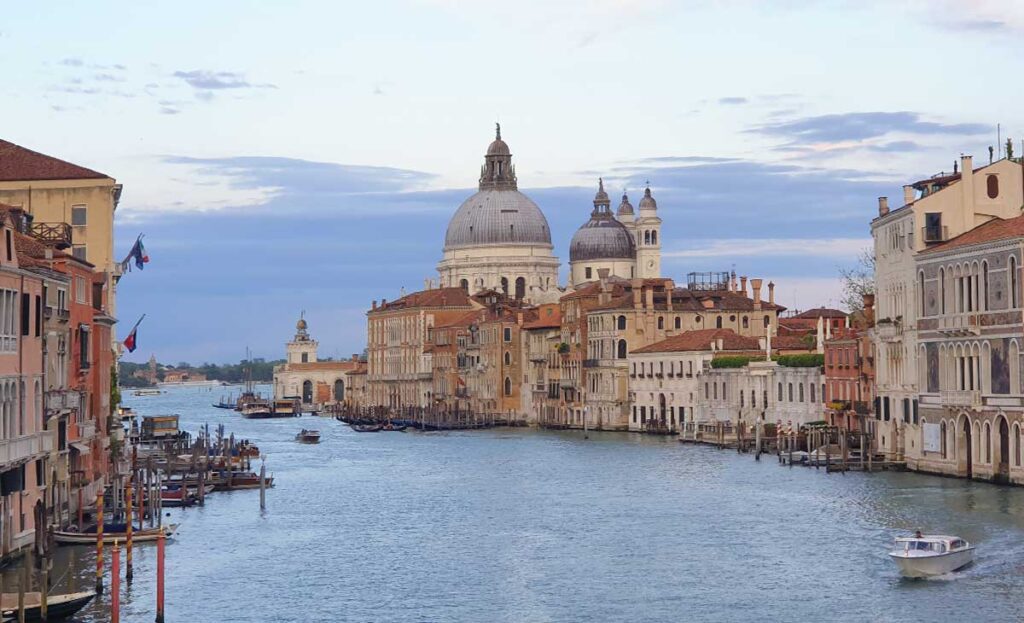 Blick über den Canal Grande in Venedig auf die markante Kuppel der Basilika Santa Maria della Salute in der Abenddämmerung.