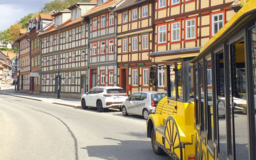 Die gelbe Bimmelbahn fährt an einer Reihe historischer Fachwerkhäuser in Wernigerode vorbei in Richtung Schloss