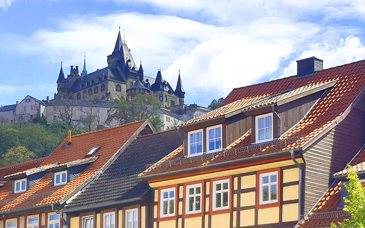 Bunte Fachwerkhäuser der Altstadt Wernigerode mit dem Schloss Wernigerode im Hintergrund unter blauem Himmel
