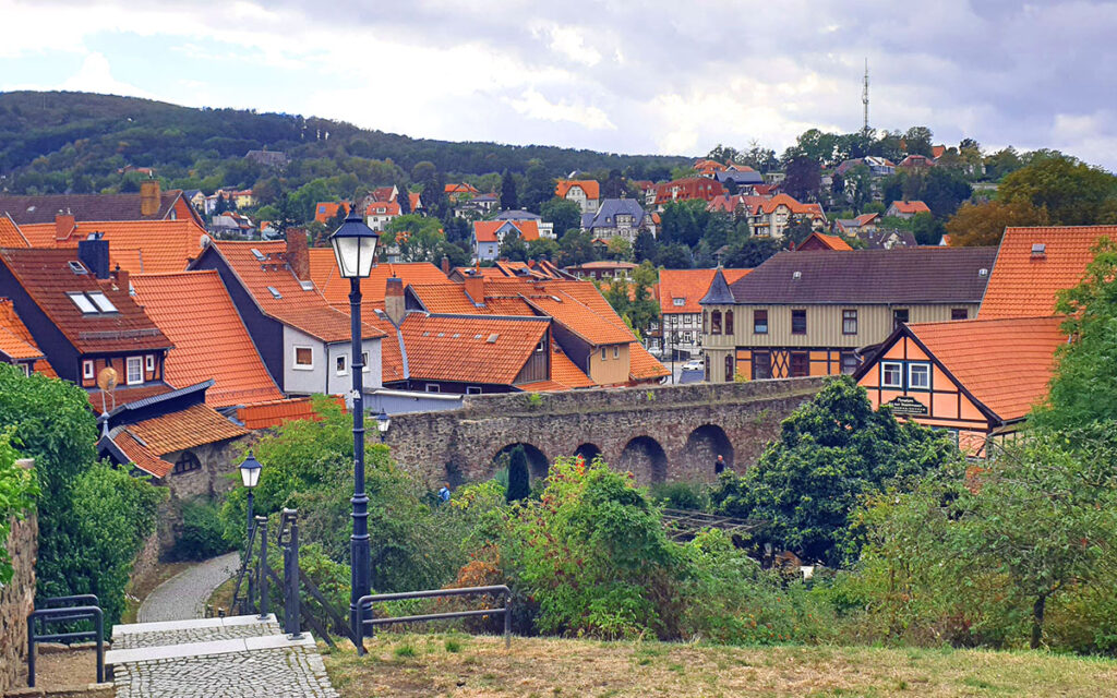 Historische Stadtmauer von Wernigerode mit Bogenfenstern, umgeben von Grünflächen und Blick auf rote Hausdächer
